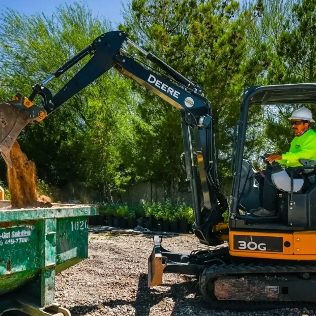Excavator loading soil into a dumpster.